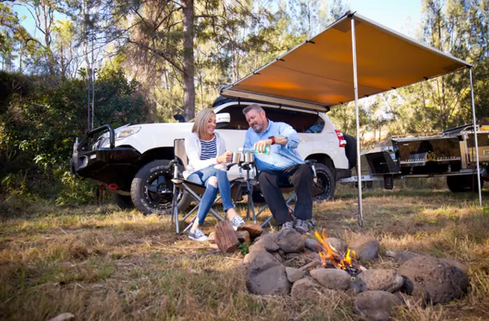 a man and woman sitting in chairs by a campfire